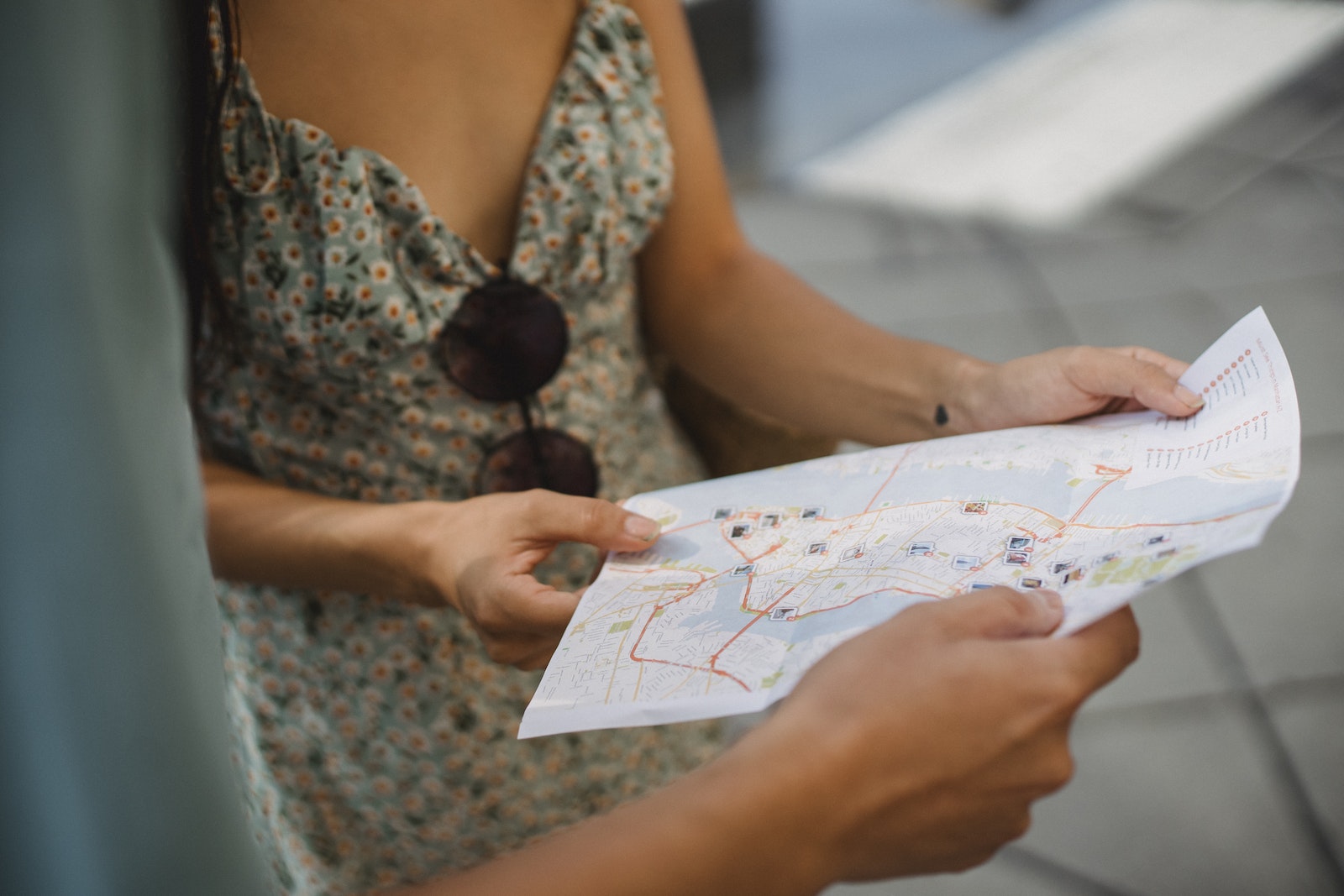 Crop anonymous couple travelers in summer clothes checking location in paper map while walking in unknown city